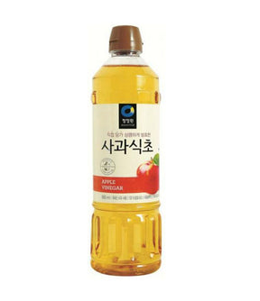 A bottle of Daesang Apple Vinegar with a label showing the product name and apple graphics, predominantly yellow liquid visible through the transparent bottle.