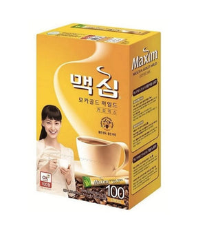 A box of Dongsuh Maxim Mocha Gold Coffee Mix featuring a picture of the product and a woman holding a cup of coffee. The packaging is predominantly yellow and the text indicates it is a 100-pack of 11.