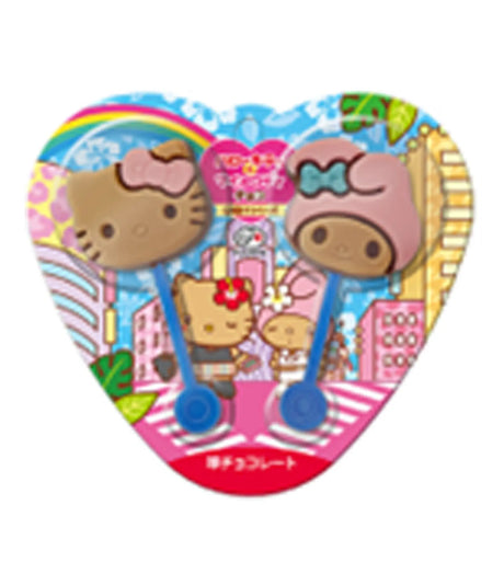 A heart-shaped Sanrio Hello Kitty product package containing two small Hello Kitty-themed items, likely hair clips or accessories, with colorful cartoon artwork on a plain white background.